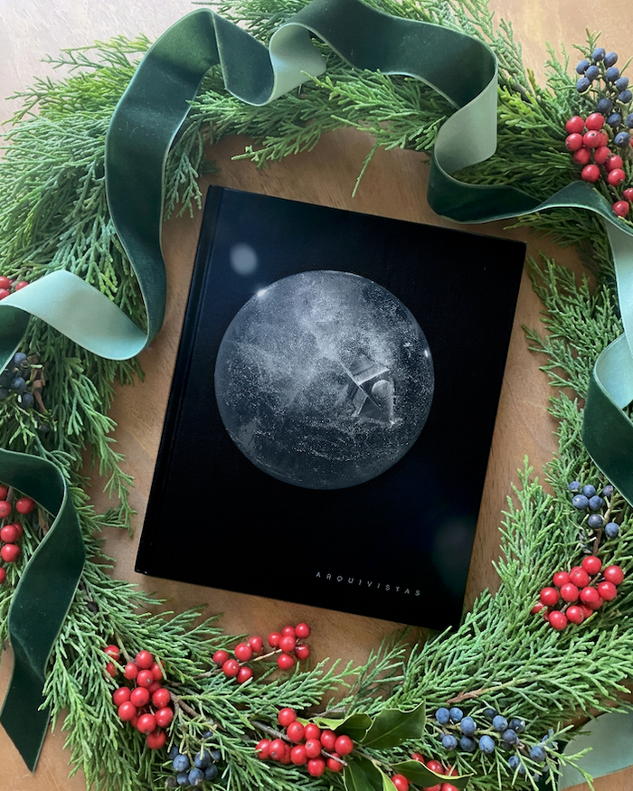 ARQUIVISTAS book surrounded by evergreen garland and velvet holiday ribbon.